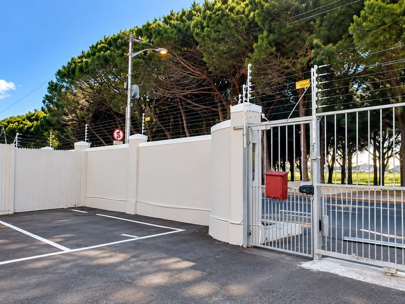 Secure apartment complex entrance featuring a paved driveway, perimeter wall with electric fencing, and a metal security gate.