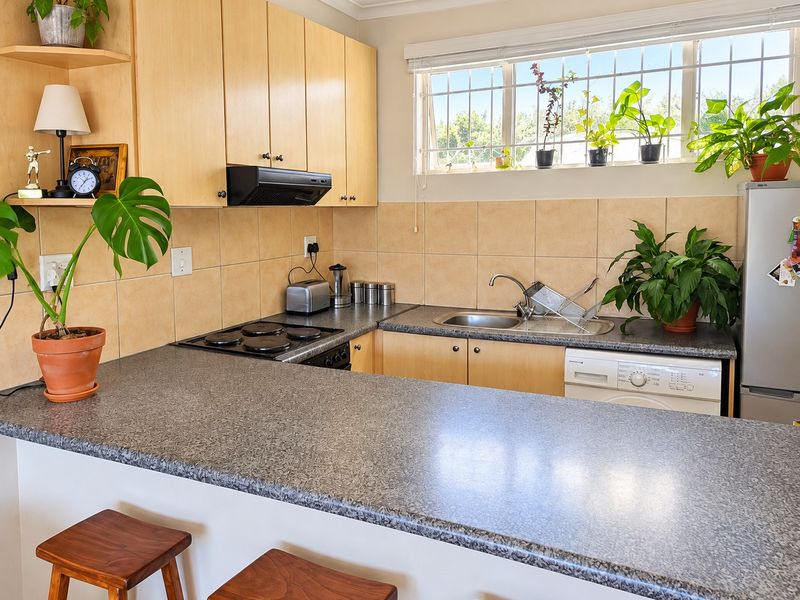 Functional kitchen featuring light wood cabinetry, laminate countertops, tiled backsplash, integrated electric hob, and a convenient breakfast bar area.