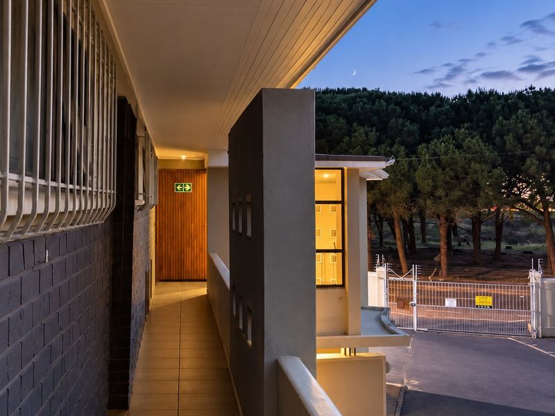 A well-maintained exterior balcony walkway featuring tiled flooring, security bars, and views of the surrounding property grounds at dusk.