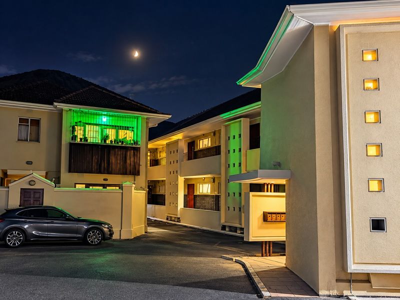 Night view of the apartment complex entrance featuring paved driveway, modern exterior lighting, and multi-level residential units with balconies.