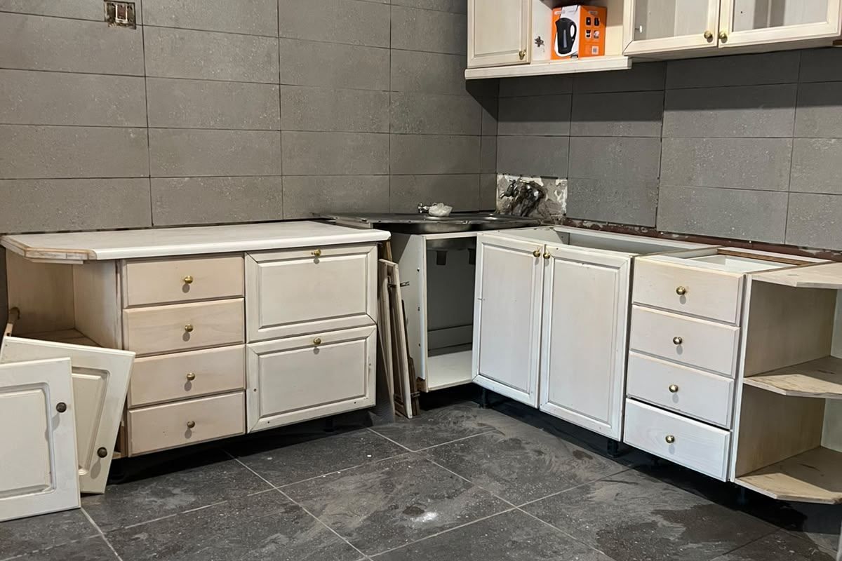 A kitchen space currently undergoing renovation, featuring installed base and wall cabinetry, tiled surfaces, and a sink, requiring completion of finishes and fixtures.