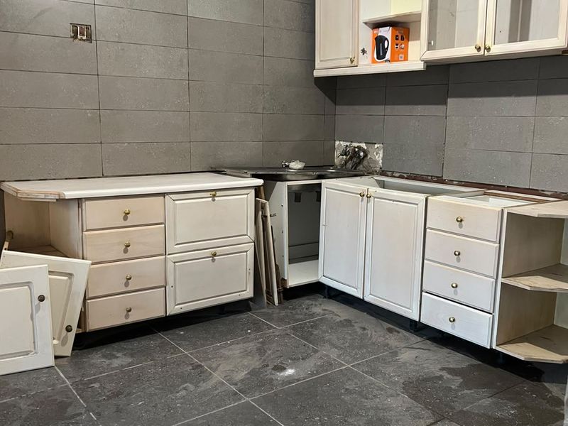 A kitchen space currently undergoing renovation, featuring installed base and wall cabinetry, tiled surfaces, and a sink, requiring completion of finishes and fixtures.