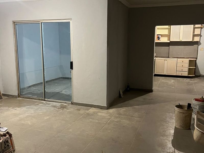 Open plan living area featuring tiled flooring, a sliding glass door, and an adjacent kitchen space with built-in cabinetry.