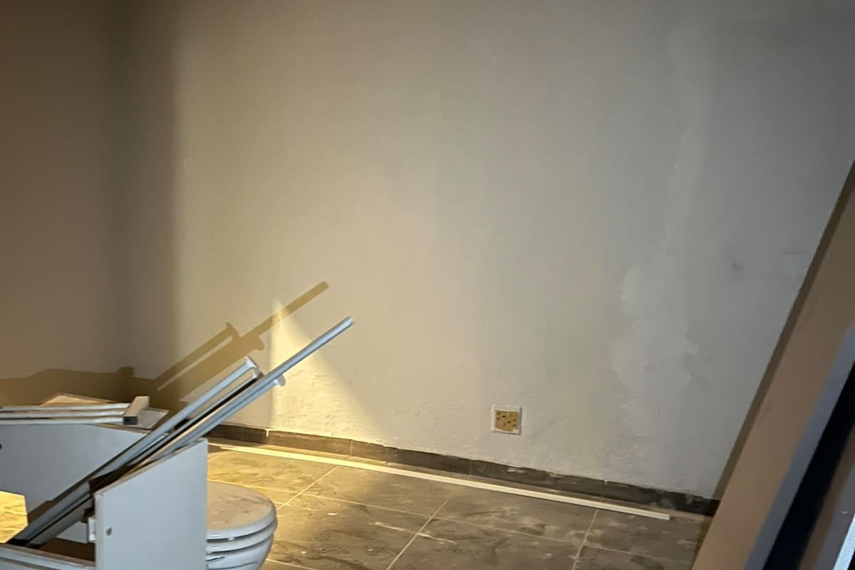 An unfinished bathroom space featuring tiled flooring and a toilet, currently undergoing renovation with exposed wall surfaces and construction debris present.