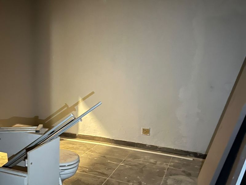 An unfinished bathroom space featuring tiled flooring and a toilet, currently undergoing renovation with exposed wall surfaces and construction debris present.