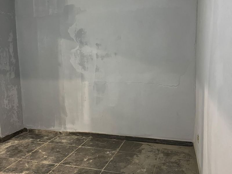 An empty room featuring tiled flooring and crown molding, currently undergoing renovation with unfinished wall surfaces and ceiling.