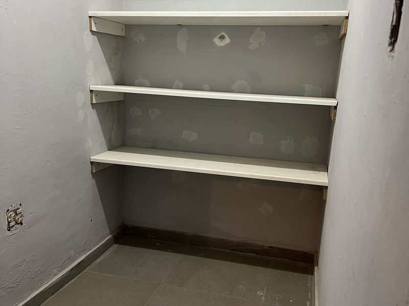 A small utility or pantry space featuring built-in shelving and tiled flooring, currently requiring wall finishing and painting to complete the interior.