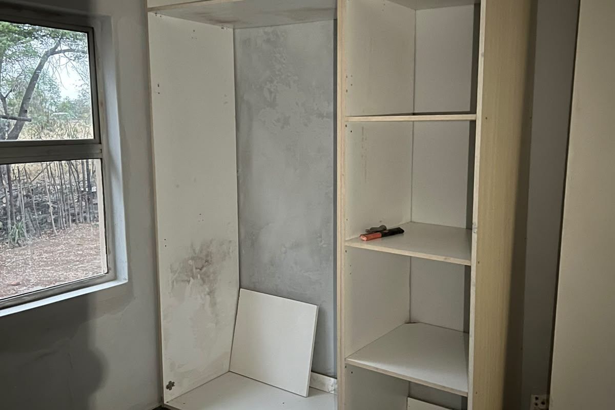 A bedroom space featuring an unfinished built-in shelving unit, tiled flooring, and a window, currently undergoing renovation or repair.