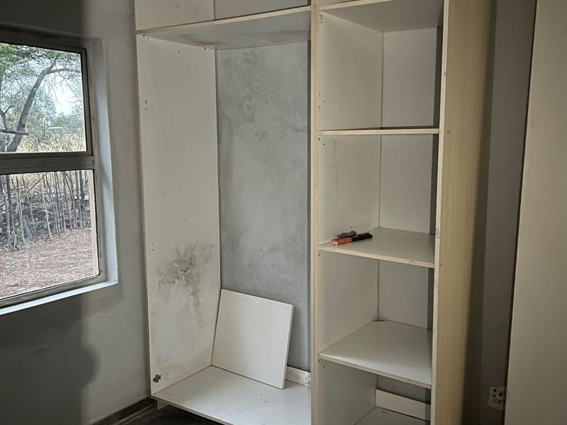A bedroom space featuring an unfinished built-in shelving unit, tiled flooring, and a window, currently undergoing renovation or repair.