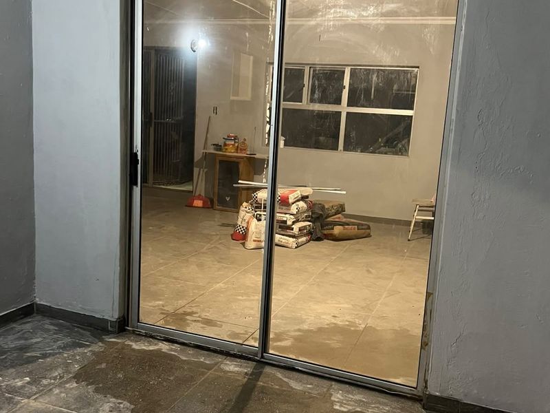 A covered patio area featuring tiled flooring and a sliding glass door, currently in a state of unfinished renovation.