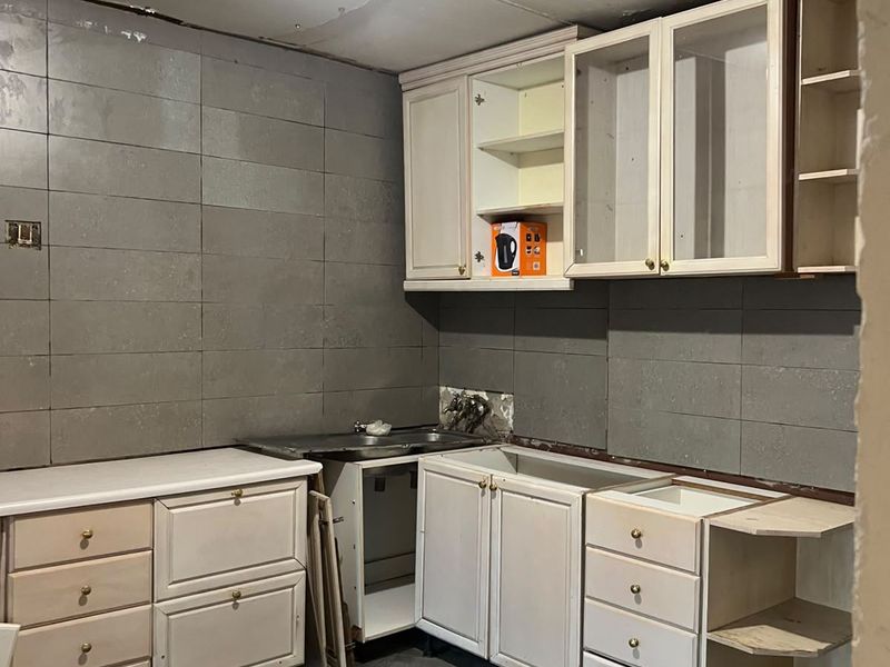 An unfinished kitchen space featuring installed cabinetry, tiled walls and flooring, and a stainless steel sink, requiring completion of countertops and ceiling finishes.
