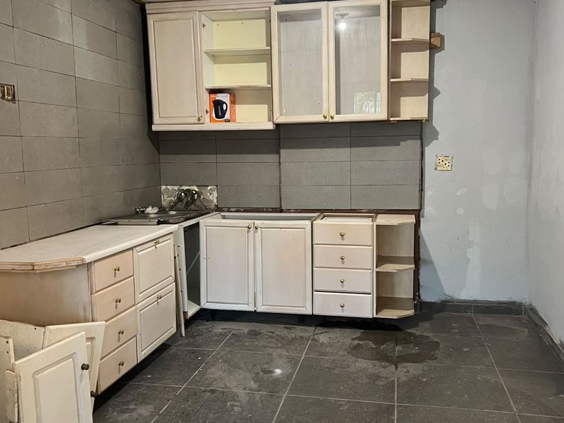 A kitchen space in need of renovation, featuring built-in cabinetry, tiled flooring, and a tiled splashback, currently showing signs of wear and incomplete finishes.