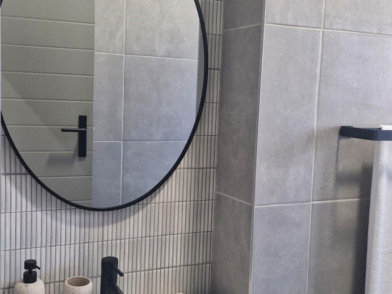 Modern bathroom featuring a sleek vanity basin with a black mixer tap, circular mirror, and contemporary grey wall tiling.