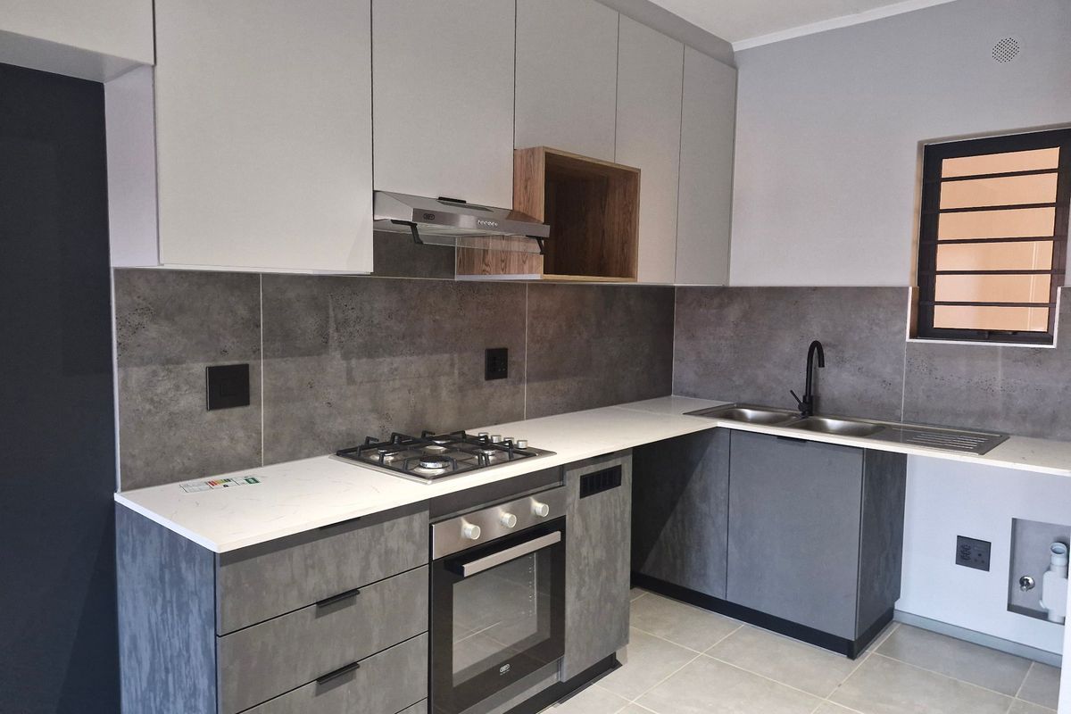 Modern kitchen featuring sleek grey cabinetry, stone countertops, a gas hob, built-in oven, extractor fan, and a double sink with a contemporary faucet.