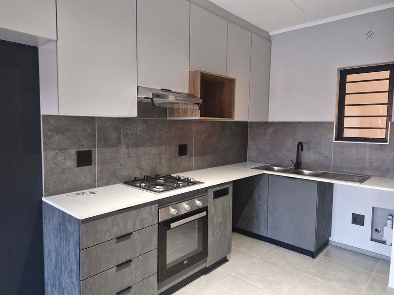 Modern kitchen featuring sleek grey cabinetry, stone countertops, a gas hob, built-in oven, extractor fan, and a double sink with a contemporary faucet.