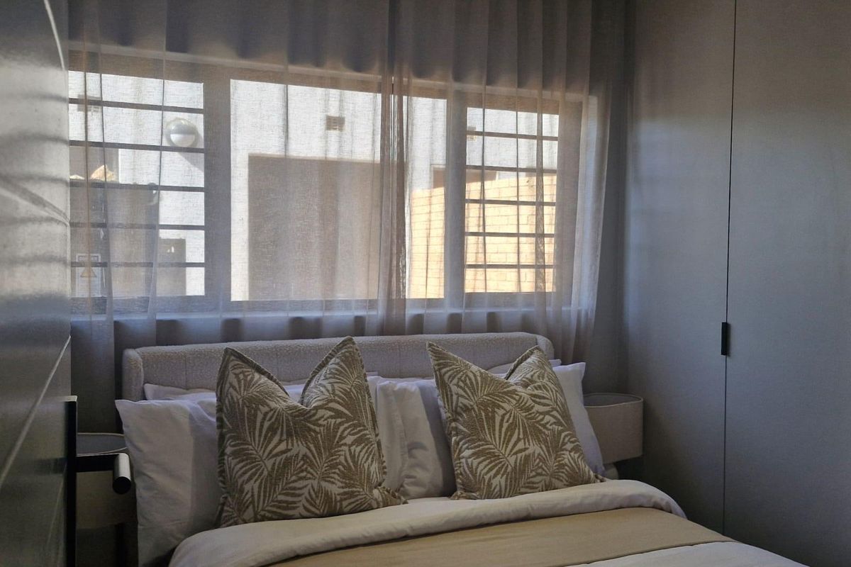 A well-lit bedroom featuring built-in cupboards and security bars on the window, providing a functional and secure living space.