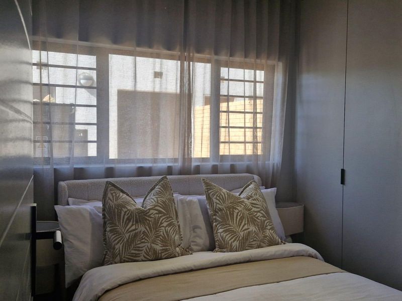 A well-lit bedroom featuring built-in cupboards and security bars on the window, providing a functional and secure living space.