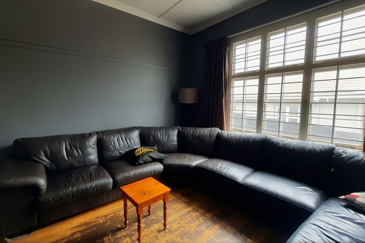 A living room featuring dark painted walls, large multi-pane windows, and original timber flooring with visible wear.