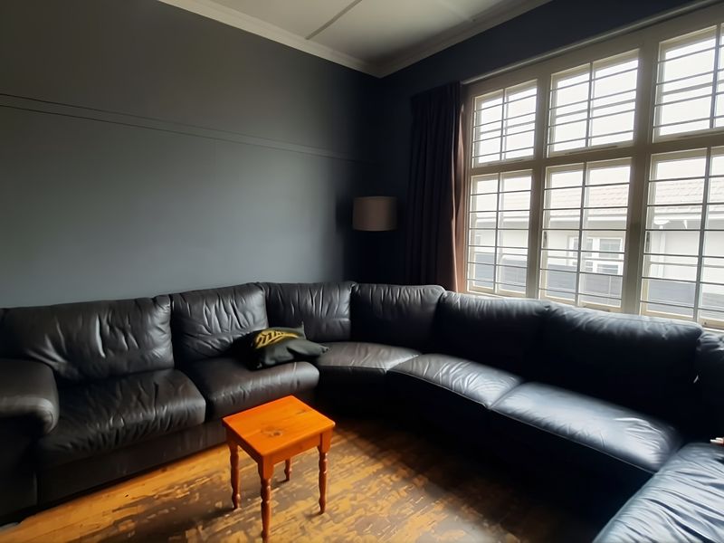 A living room featuring dark painted walls, large multi-pane windows, and original timber flooring with visible wear.