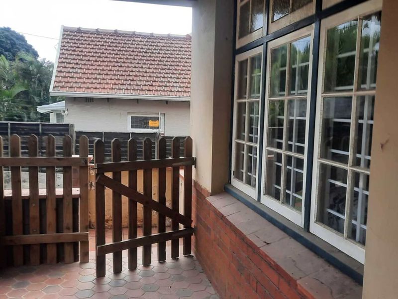 A covered patio area featuring brick paving, a timber picket gate, and multi-pane timber windows set into a brick base.