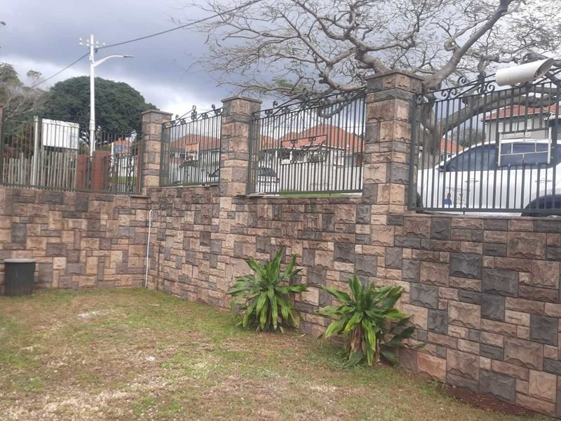 A rear garden area featuring a decorative stone-clad retaining wall, wrought iron security fencing, and a water storage tank.
