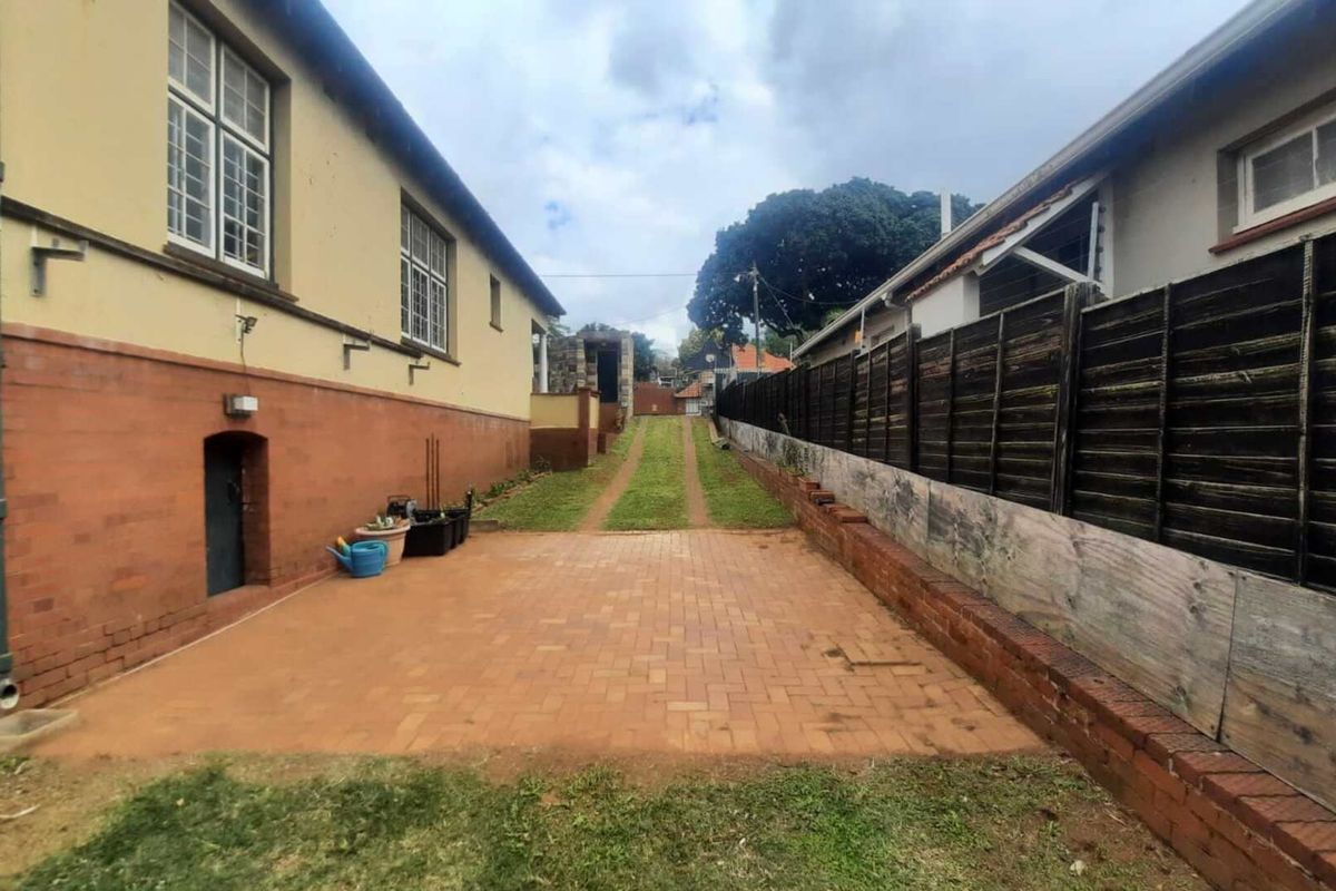 Rear exterior view featuring a brick paved area, grass driveway, and timber boundary fencing between two properties.
