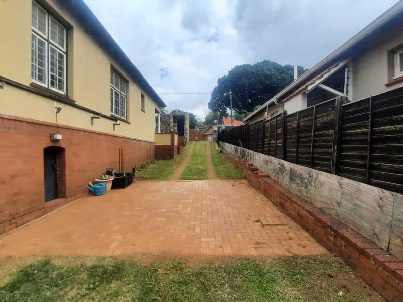 Rear exterior view featuring a brick paved area, grass driveway, and timber boundary fencing between two properties.