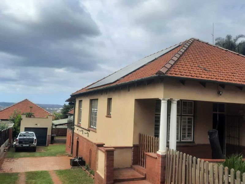 Front elevation of a traditional house featuring a terracotta tile roof with solar panels, a covered veranda with columns, and a paved driveway.