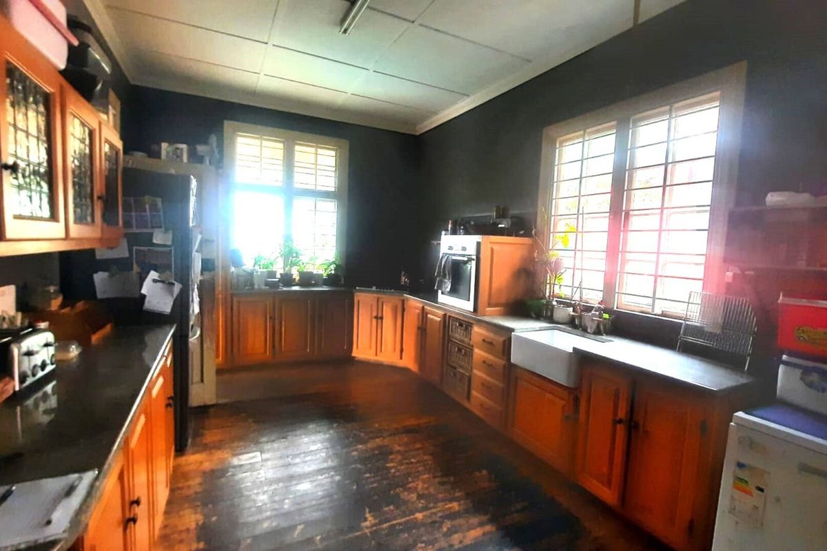 A spacious kitchen featuring timber cabinetry, a farmhouse sink, and built-in oven, with large windows providing natural light and security bars.