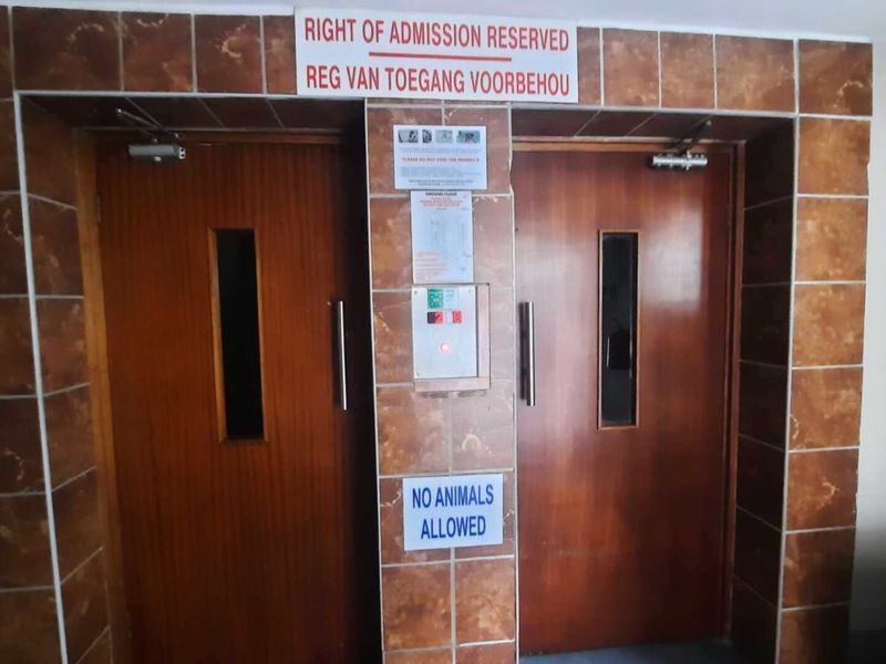 A functional elevator lobby area featuring wood-finish doors and tiled wall surrounds within an apartment building.