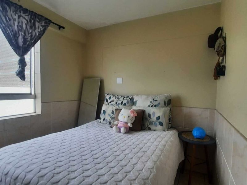 A compact bedroom featuring tiled wall wainscoting and a large window, providing a functional space with neutral finishes.
