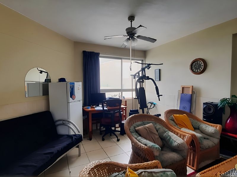 A living room featuring tiled flooring, a ceiling fan, and a large sliding window providing natural light.
