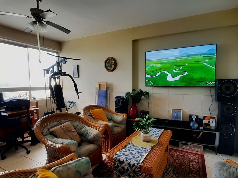 A living room featuring tiled flooring, a ceiling fan, and a tiled feature wall with a large wall-mounted television.