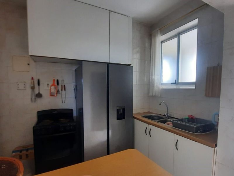 A functional kitchen featuring built-in cabinetry, a double basin sink, tiled splashbacks, and a sliding window for natural light.