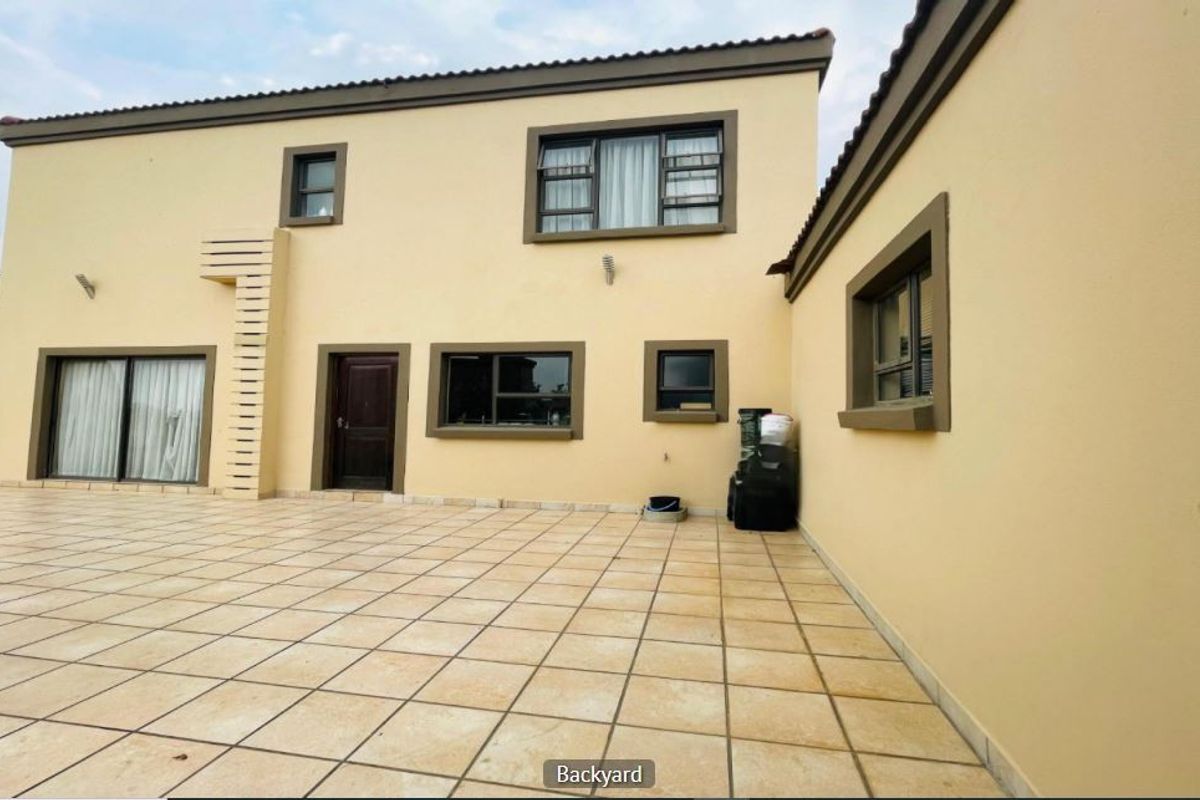 A spacious rear exterior view featuring a large tiled patio area, sliding glass doors, and well-maintained exterior walls with aluminium window frames.