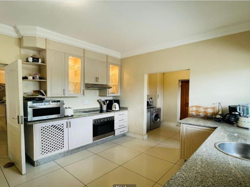 A functional kitchen featuring light-toned cabinetry, granite countertops, built-in oven, and tiled flooring, with an adjacent utility area visible.