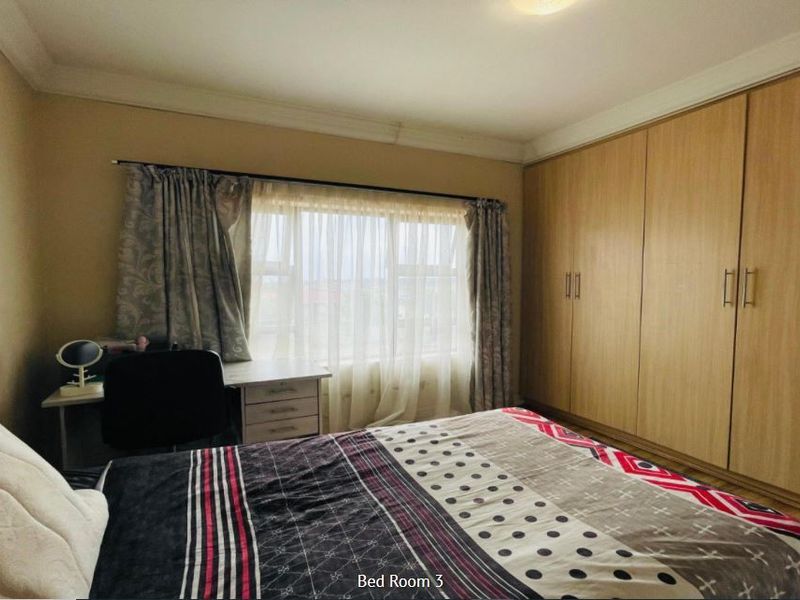 A bedroom featuring built-in wooden cupboards, neutral wall finishes, and a window with curtain treatments.