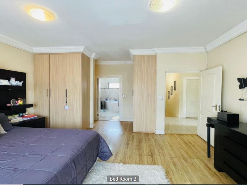 Spacious bedroom featuring light wood laminate flooring, built-in cupboards, and crown molding, with direct access to an en-suite bathroom and hallway.