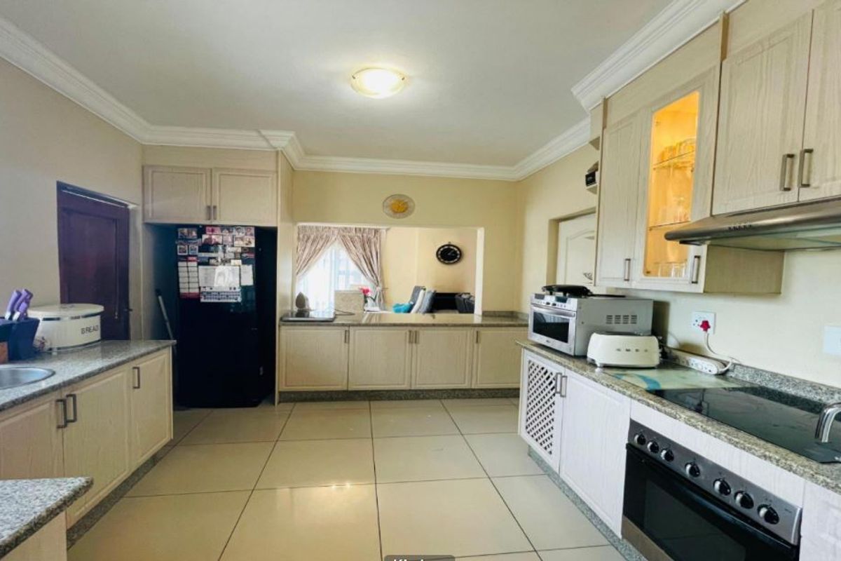 A functional kitchen featuring light-toned built-in cabinetry, granite countertops, integrated oven and hob, and tiled flooring with a convenient pass-through to the living area.