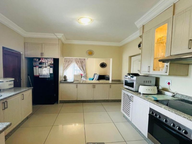 A functional kitchen featuring light-toned built-in cabinetry, granite countertops, integrated oven and hob, and tiled flooring with a convenient pass-through to the living area.