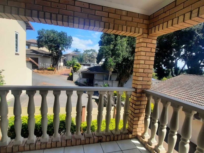 A covered balcony featuring brick pillars and a concrete balustrade, offering an elevated view of the surrounding residential neighbourhood.