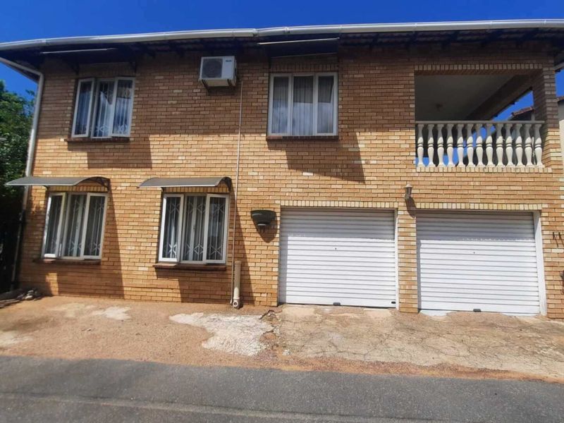 Front elevation of a double-story face brick townhouse featuring a double garage, upper-level balcony with balustrade, and security bars on windows.