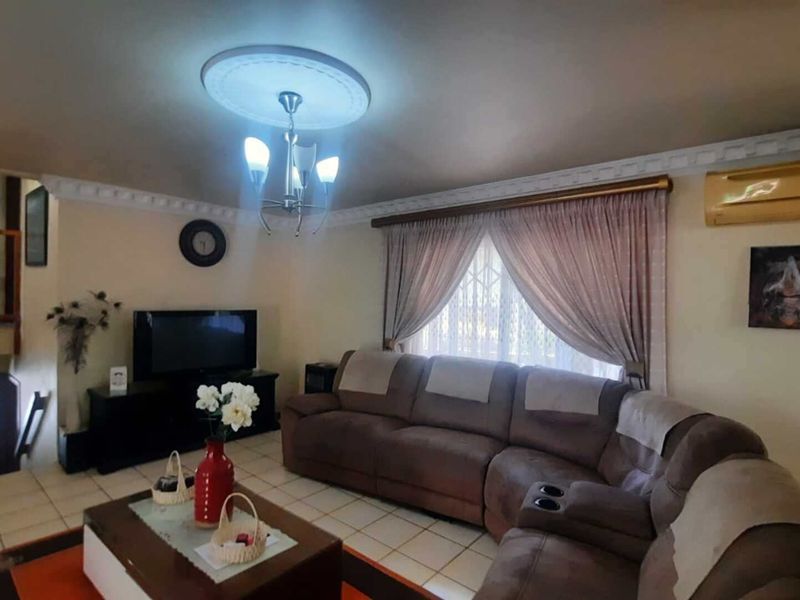 A comfortable living room featuring tiled flooring, decorative coving, a ceiling rose, and a wall-mounted air conditioning unit.