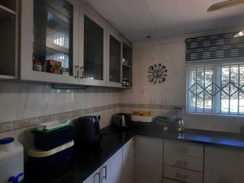 Functional kitchen featuring built-in cabinetry, dark granite countertops, and a tiled backsplash with a window fitted with security bars.