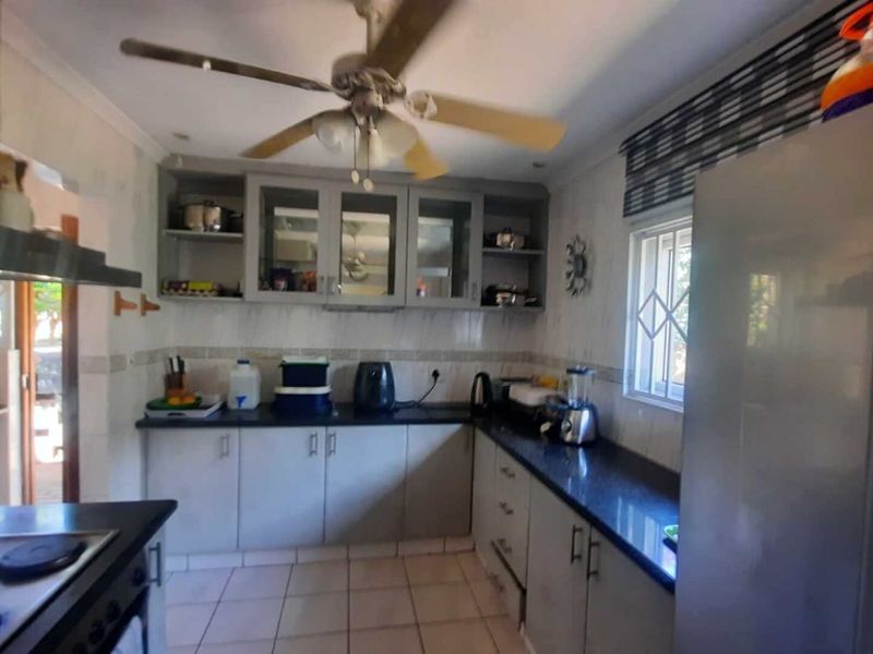 Functional kitchen featuring built-in cabinetry, granite countertops, tiled flooring, and a ceiling fan, offering a practical layout for daily meal preparation.
