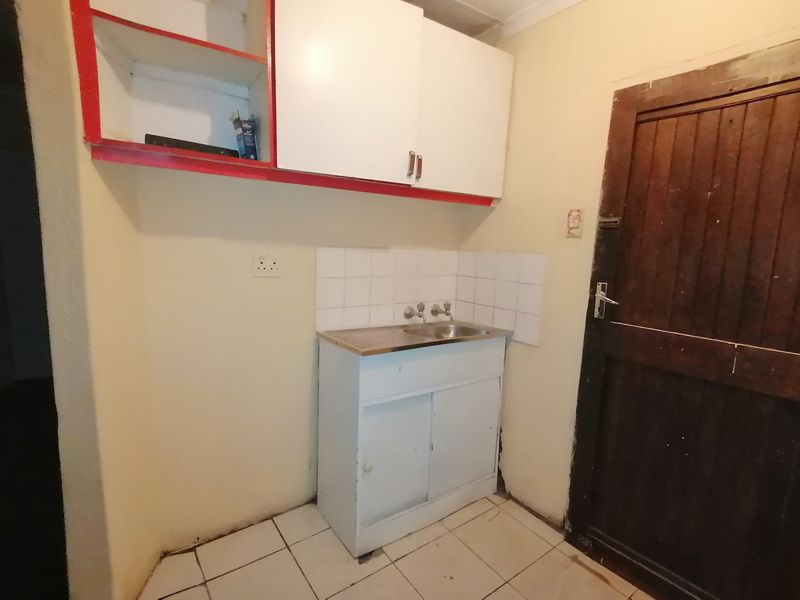 A compact scullery or utility area featuring a stainless steel sink, tiled splashback, and basic built-in cabinetry.