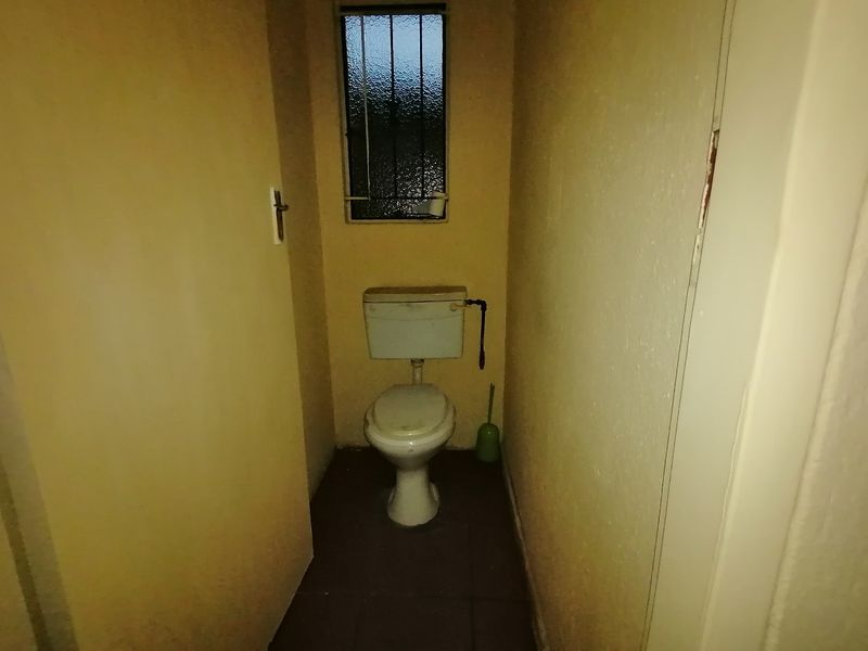 A small, functional guest toilet featuring tiled flooring and a window with security bars, requiring cosmetic updates to modernize the space.