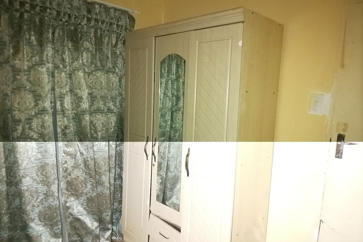 A bedroom interior featuring a built-in wardrobe with a mirror, showing signs of wear on the surrounding wall surfaces.