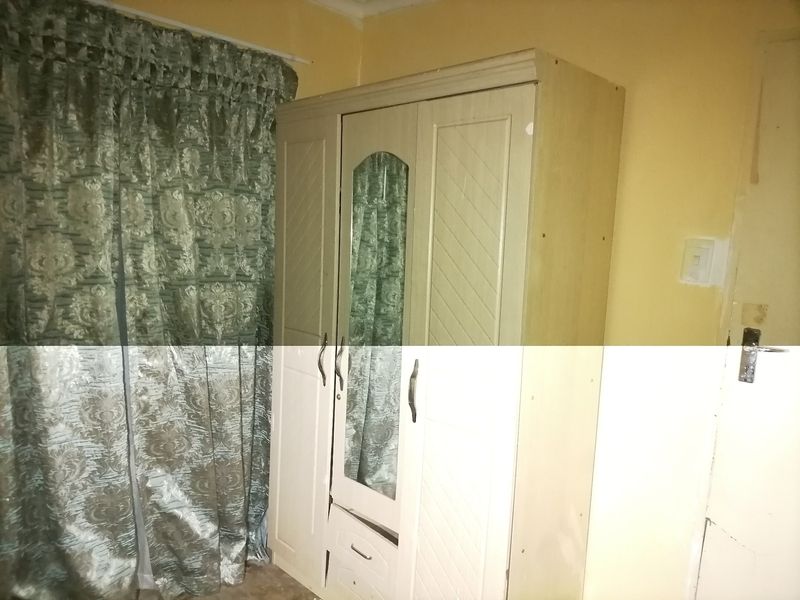 A bedroom interior featuring a built-in wardrobe with a mirror, showing signs of wear on the surrounding wall surfaces.