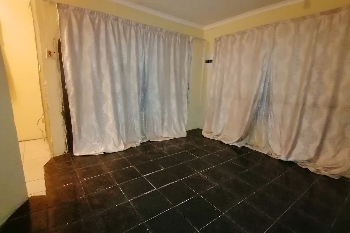 An empty living room featuring dark tiled flooring and sliding glass doors, requiring minor cosmetic repairs to the wall plaster.